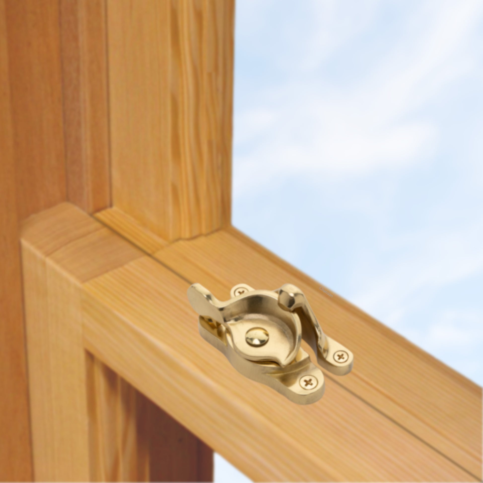 A wooden sash window, single or double hung, with a large solid brass sash catch or latch installed on the meeting rail, shown in unlacquered brass