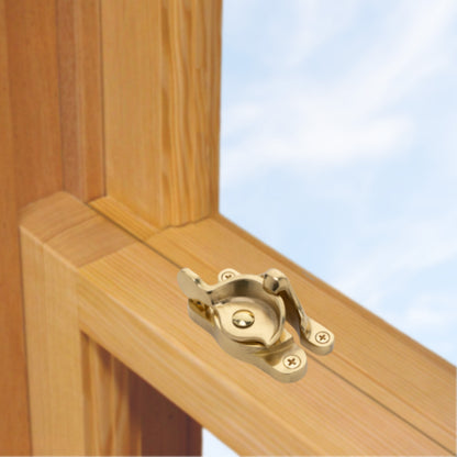 A wooden sash window, single or double hung, with a large solid brass sash catch or latch installed on the meeting rail, shown in unlacquered brass